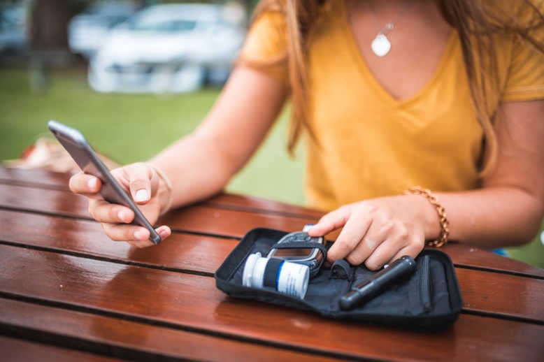 Young woman measuring blood sugar level and using mobile phone